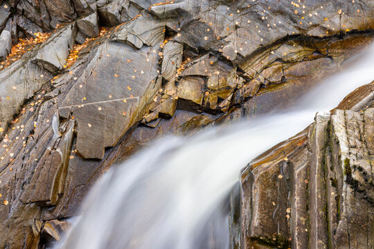 Close-up of cascading water at the Falls of Bruar, Scotland—smooth flow over layered rock formations framed by autumn leaves and Highland forest textures