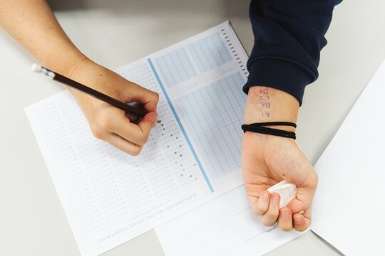 Person taking a test, filling answers on a sheet. Test-taking, exam, pencil in hand. Focus on test, exam sheet, and pencil. Test-taking scene, exam setting. Cheating on school exams.