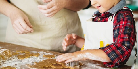Child and adult baking together, using cookie cutters on dough. Hands covered in flour, wearing aprons. Baking, cookies, and family fun in the kitchen. Baking activity for kids with copy space.