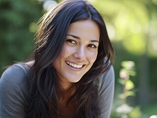 Fototapeta premium A beautiful woman with long dark brown hair and a big smile. In the soft natural light, the background is greenery.