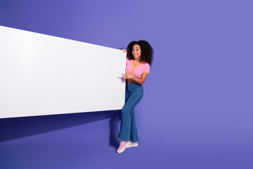 Stylish young woman posing on vivid violet background with an engaging smile while interacting with...