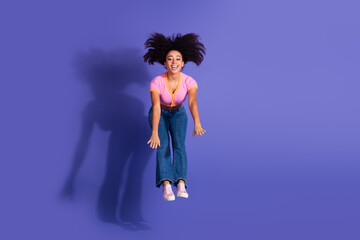 Joyful young woman jumping energetically in stylish casual attire against a vibrant purple...