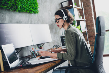 Young female programmer working remotely in a stylish home office with dual monitors, coding...