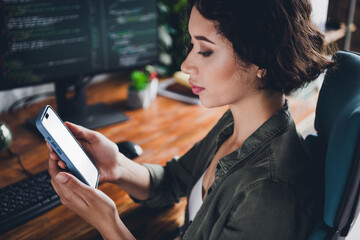 Female programmer using smartphone while working at her desk, coding on a computer in a stylish...