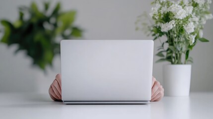 Obraz premium Laptop resting on a table, hands covering the screen, plants and flowers in the background