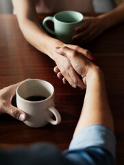 Close-up of a handshake over coffee. Two people with coffee cups, shaking hands. Handshake and coffee meeting. Hands and coffee cups on a wooden table. Casual business agreement through handshake.