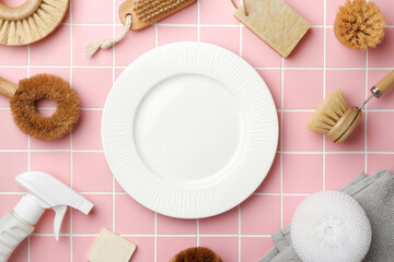 A white plate with spray bottle, eco friendly cleaning brushes for washing dishes, soap and sponge on pink tile. Cleaner concept mockup. Copy space.
