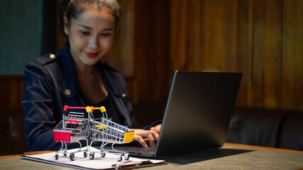Two shopping carts placed on documents in front of business owner is working on laptop and looking at it, online marketing business