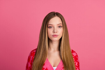 Fototapeta premium Portrait of a young woman with natural makeup and long blond hair posing stylishly in a pink cardigan against a pink background