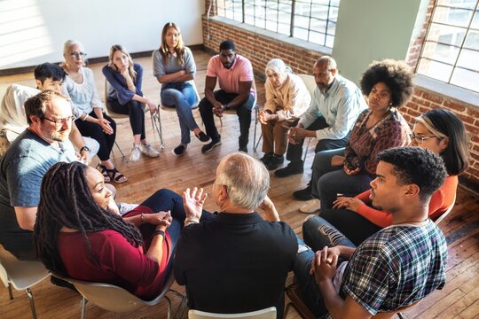 Diverse group in a circle, discussing in a bright room. Mixed genders, engaged in conversation, sharing ideas, and listening attentively. Diverse people sitting in a circle of support from community.