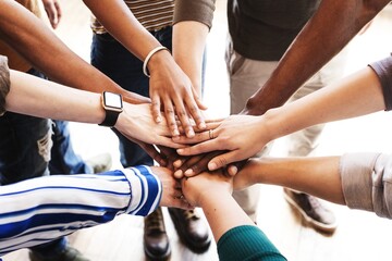 Diverse group of people with hands together in unity. Hands of different ethnicities and genders in a circle. Teamwork and unity shown through hands in a group. Team stacking hands together.
