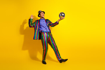 Colorful young man in a retro-style disco outfit holding a sparkling ball against a bright yellow background, enjoying himself