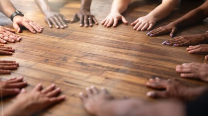 Diverse hands of various ethnicities on wooden floor. Unity and teamwork shown by hands. Hands of different genders and ethnicities symbolizing collaboration and unity. Group workout on floor.