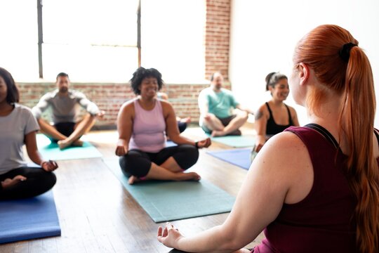 Diverse group of men and women practicing yoga. The yoga class includes various ethnicities, with participants sitting on yoga mats. Yoga for relaxation and fitness. Exercise and yoga for well being.