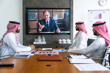 Arab businessmen wearing saudi kandura meeting in office for business deal - Corporate business group of middle-eastern people working in an international company in middle east