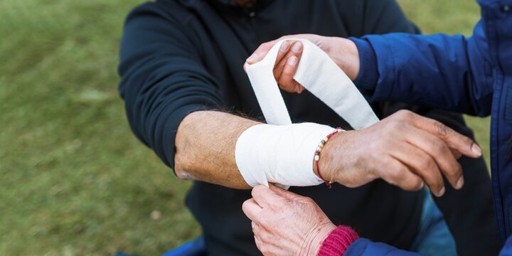 Close-up of a person bandaging another's arm outdoors. Focus on hands and bandage. Arm bandaging, first aid, and care in a natural setting. Man with injured arms while on hike in nature.