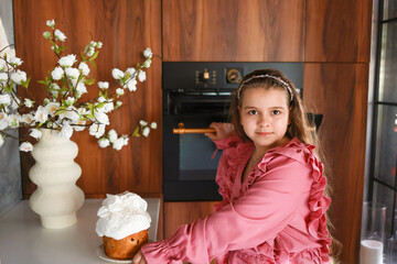 A cute girl in a pink dress baked an Easter cake. Family traditions