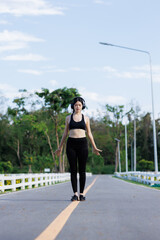 Fototapeta premium An Asian female runner enjoys her evening jog in a peaceful outdoor park, smiling as she moves with the rhythm of the fading sunlight.