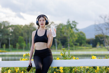 A young female runner pauses to catch her breath, takes a sip of water, and scrolls through her...