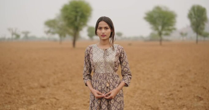 Indian young adult gen z farmer woman wear casual dress cross arms outdoor farmland looking at camera asian happy smiling village teen age girl fold hand posing for cam outside ground