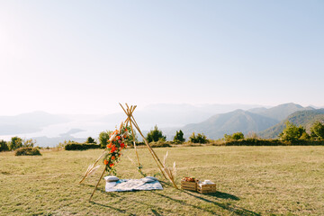 Wedding arch in the form of an Indian wigwam stands on a green lawn in the mountains