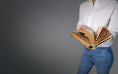 The image shows the upper torso of a man dressed in a white shirt and blue jeans holding an open book. The image focuses on the book, highlighting its pages as if the man is reading it. The background