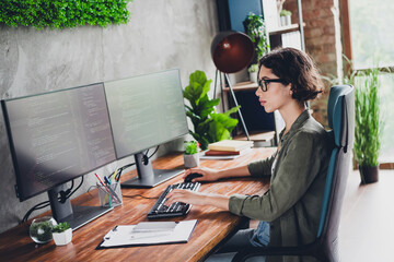 Young female programmer working remotely at her home office on multiple screens with coding...