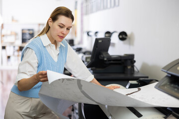 Caucasian woman working in printing office, using large format printer.