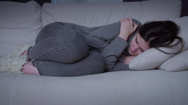 A frustrated young woman in her 20s is immersed in sad thoughts, thinking, looking away, feeling tense and unhappy. Hugs herself .Teenage problems, insecure teenager has life problems.