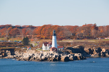 Portland Head Light in Cape Elizabeth, Maine as seen from the Atlantic Ocean on an autumn morning with trees in fall colors. An historic 1791 lighthouse still in operation.