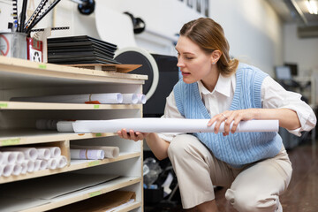 Positive woman employee at copy center putting roll paper on shelves