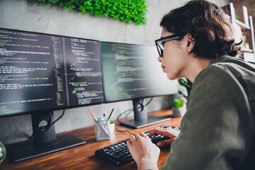 Young female programmer working at home office coding software on dual monitors in a relaxed and professional workspace setting