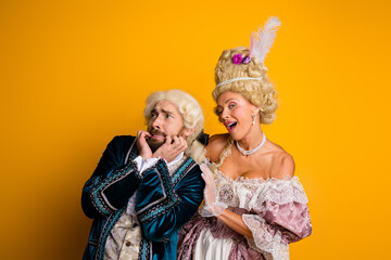 Two individuals wearing vintage era noble costumes posing joyfully against a bright yellow background