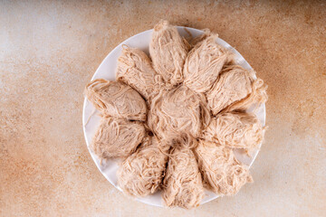 Traditional Asian sweets Pishmaniye, also known as Pashmak, Dragon's Beard, or Kkul Tarae, thread-like hair halvah, with nutty flavor, on a plate, copy space