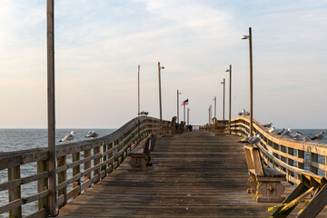 Seagulls perch on Oak Island Fishing Pier in North Carolina, overlooking calm ocean waters under early morning sky.