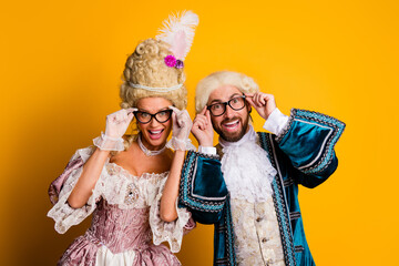 Elegant couple in historic costumes poses with glasses against yellow backdrop