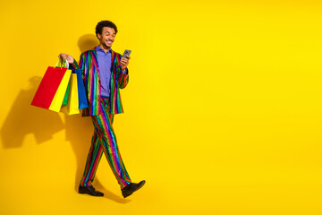 Charismatic young man in a colorful suit holding shopping bags against a yellow background,...