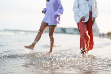 Two Female Friends Walking Barefoot on a Beach at Sunset in Warm Golden Light