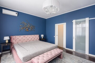 Elegant bedroom with blue walls, a plush pink bed, a decorative golden tree, and a chandelier.