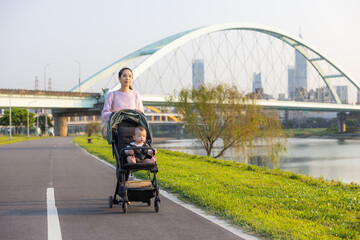 Mum walking with baby on stroller at river park