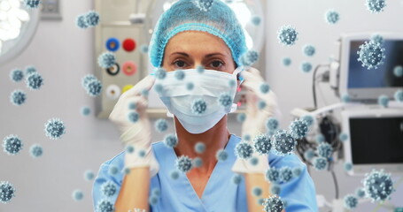 Image of caucasian female doctor with face mask over virus cells