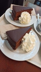 Two slices of chocolate cake with whipped cream served on white plates in a cafe. Concept of dessert indulgence, sweet treat and enjoying traditional pastry in a relaxed setting