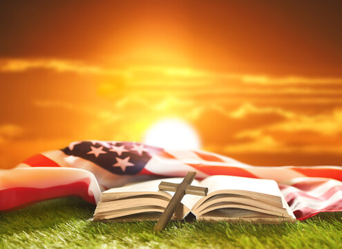 Holy Bible, Christian cross and US flag on grass. Sunny day. God Bless America.