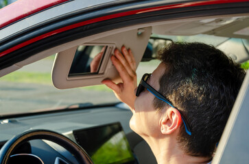 woman looks in the car mirror and adjusts the sun visor while sitting in the car wearing sunglasses