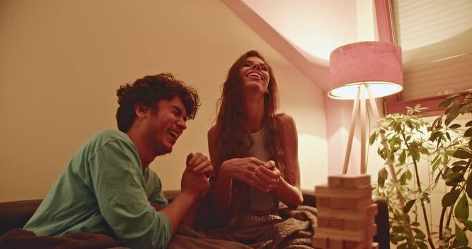 Young couple playing a game of Jenga, enjoying their time together. The warm lighting creates a cozy and intimate atmosphere.