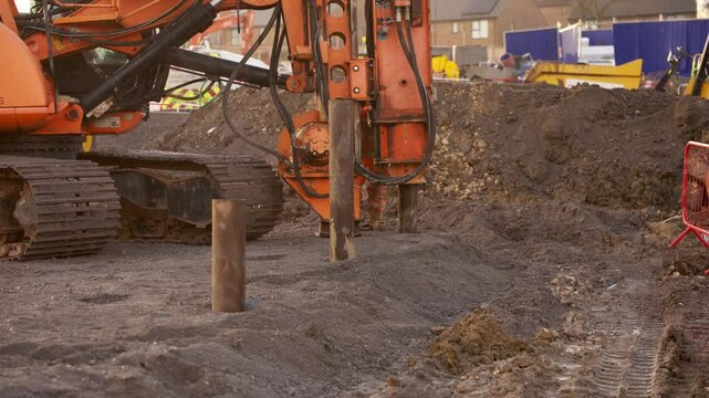 Driving rig piler machine pushing steel tubular pile deep into ground as part of foundation works