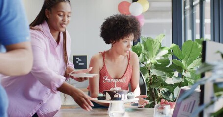 Diverse coworkers handing farewell cake in office at office amid colorful balloons