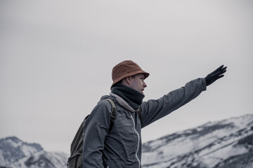 Young man pointing to the horizon to be a guide. Cold environment with snowy mountains.