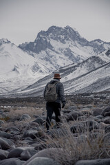 A river with stones on the bank and snow-capped mountains in the background. A cold atmosphere.