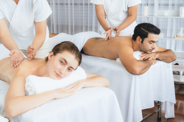 Caucasian couple customer enjoying relaxing anti-stress spa massage and pampering with beauty skin recreation leisure in day light ambient salon spa at luxury resort or hotel. Quiescent